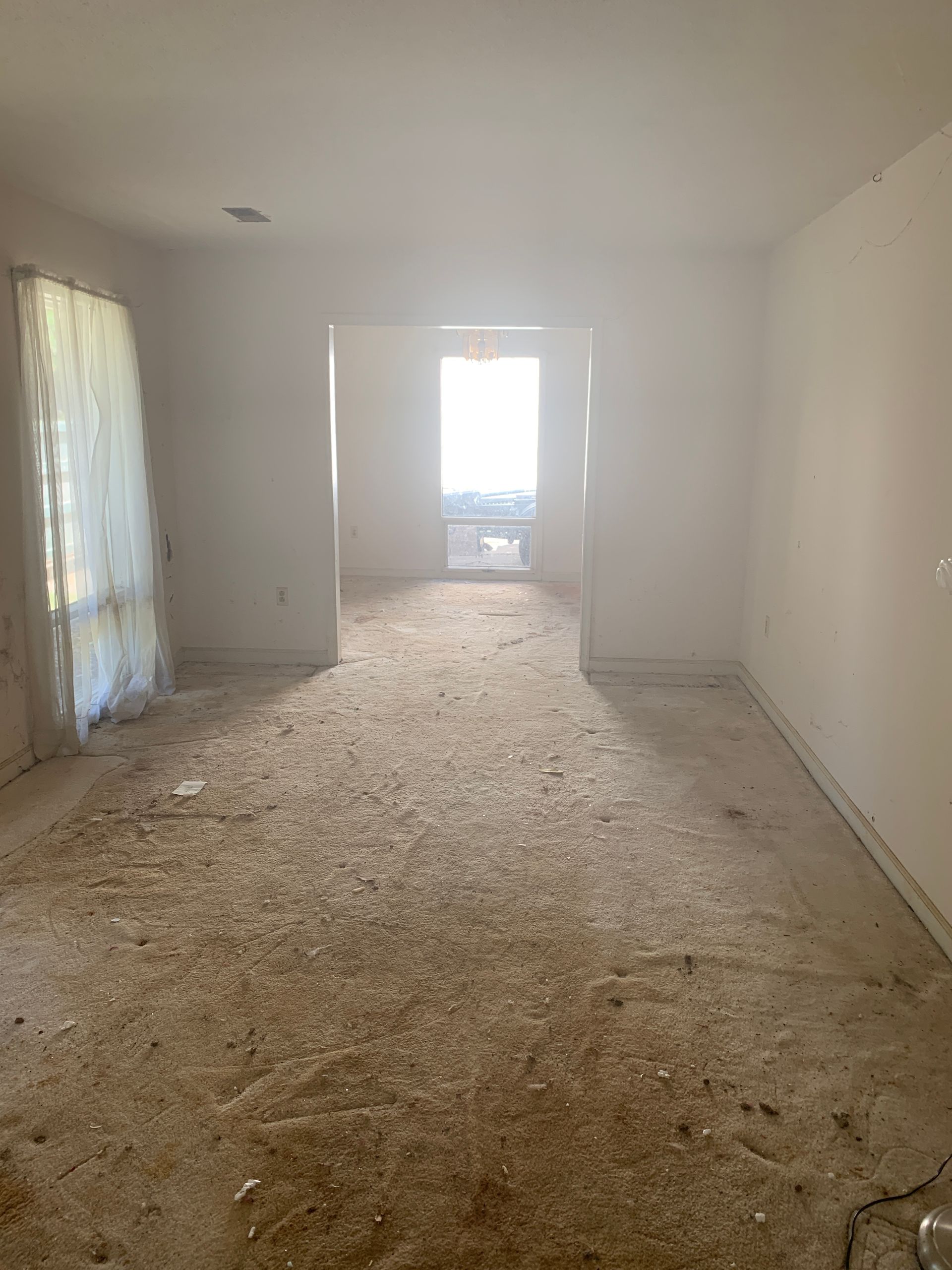 Empty room with debris on the floor, opening to a brighter area with a window.