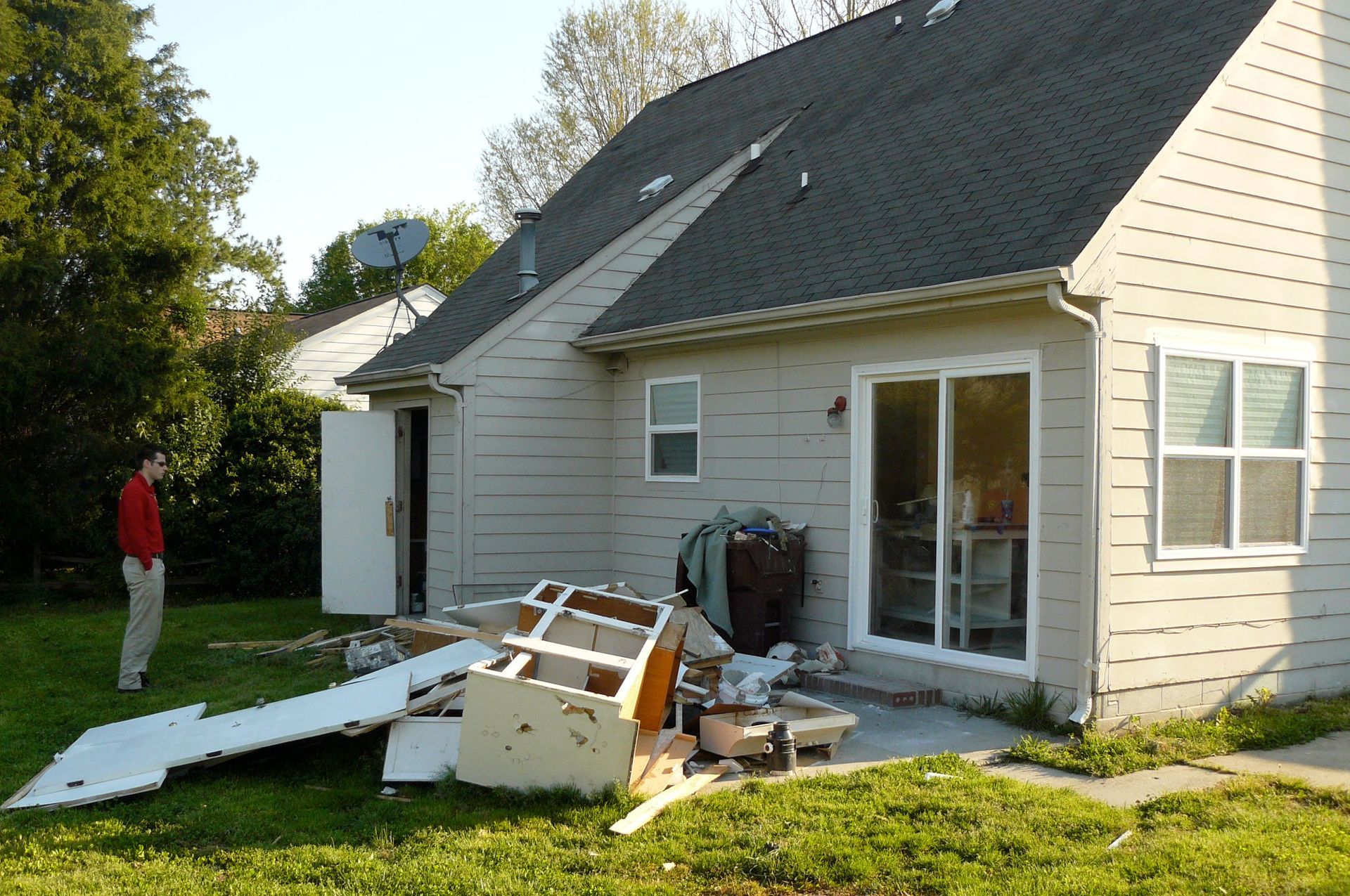 A person stands near a house with debris on the lawn.