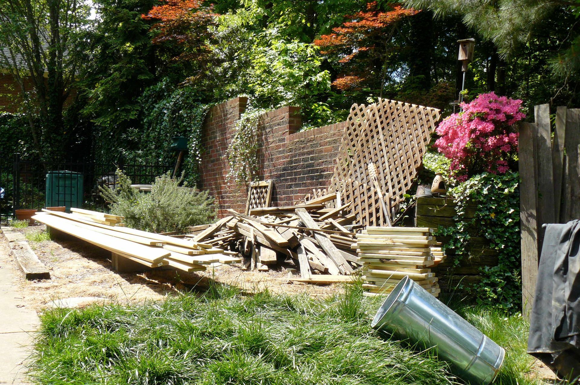 Backyard scene with construction debris, brick wall, plants, and fallen metal cylinder.