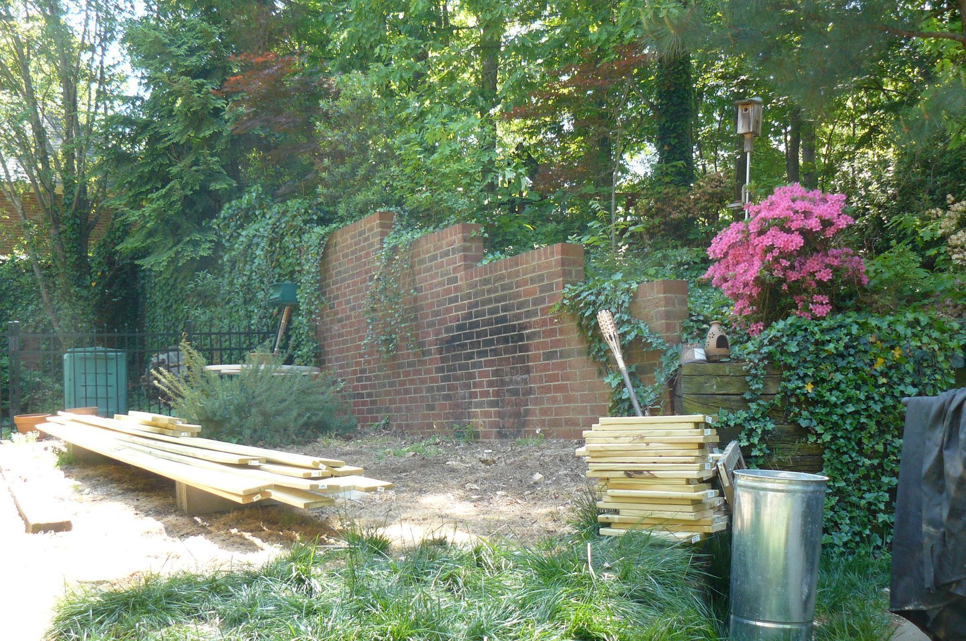 Brick wall with ivy, wood planks, trees, and pink flowers in an outdoor setting.