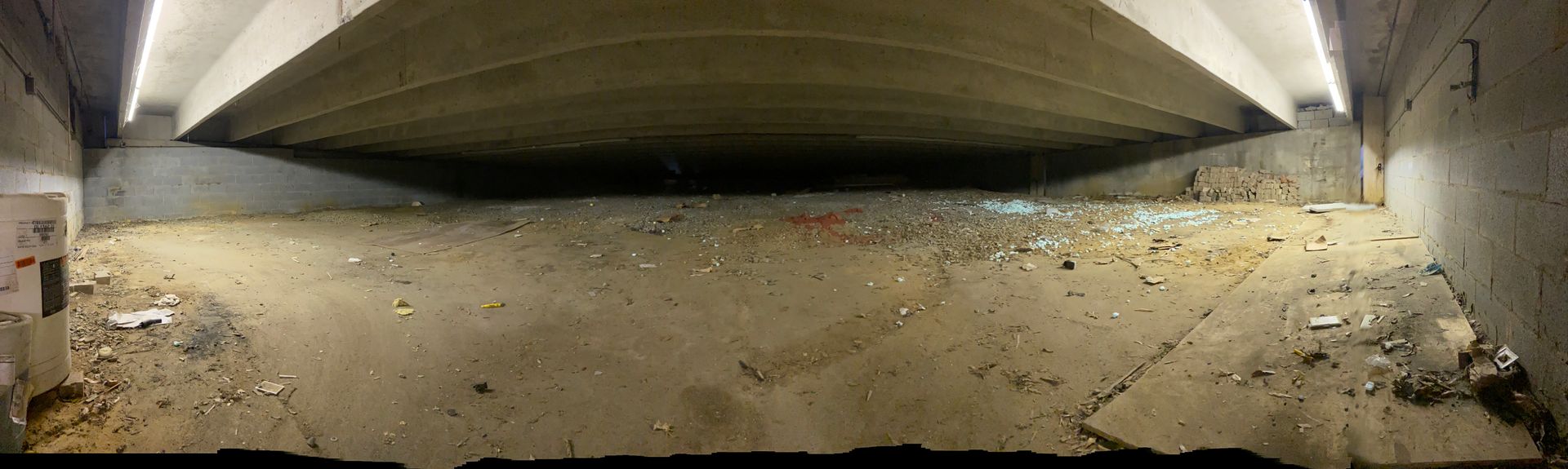 Underpass with concrete ceiling and walls, debris scattered on the ground. Lighting fixtures illuminate the structure.