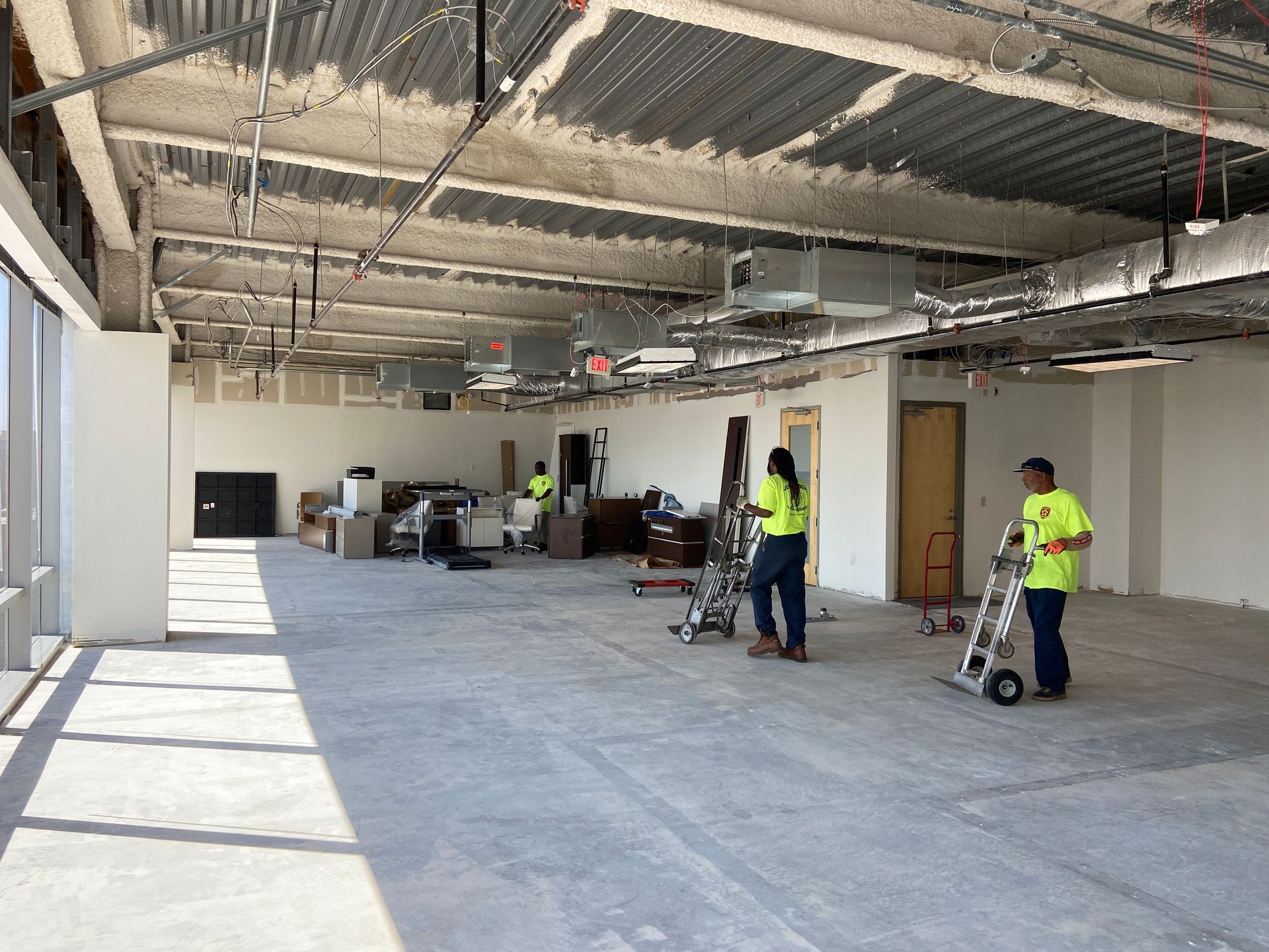 Construction site: Workers with equipment in unfinished office space with exposed ceiling and large windows.