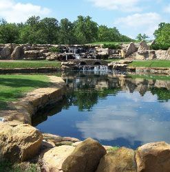 A pond with a waterfall in the background and trees reflected in the water.
