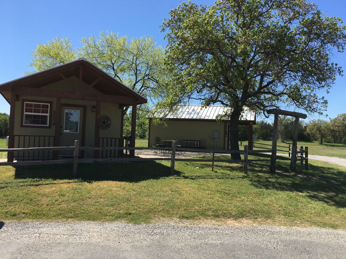 A small cabin with a porch in the middle of a grassy field.