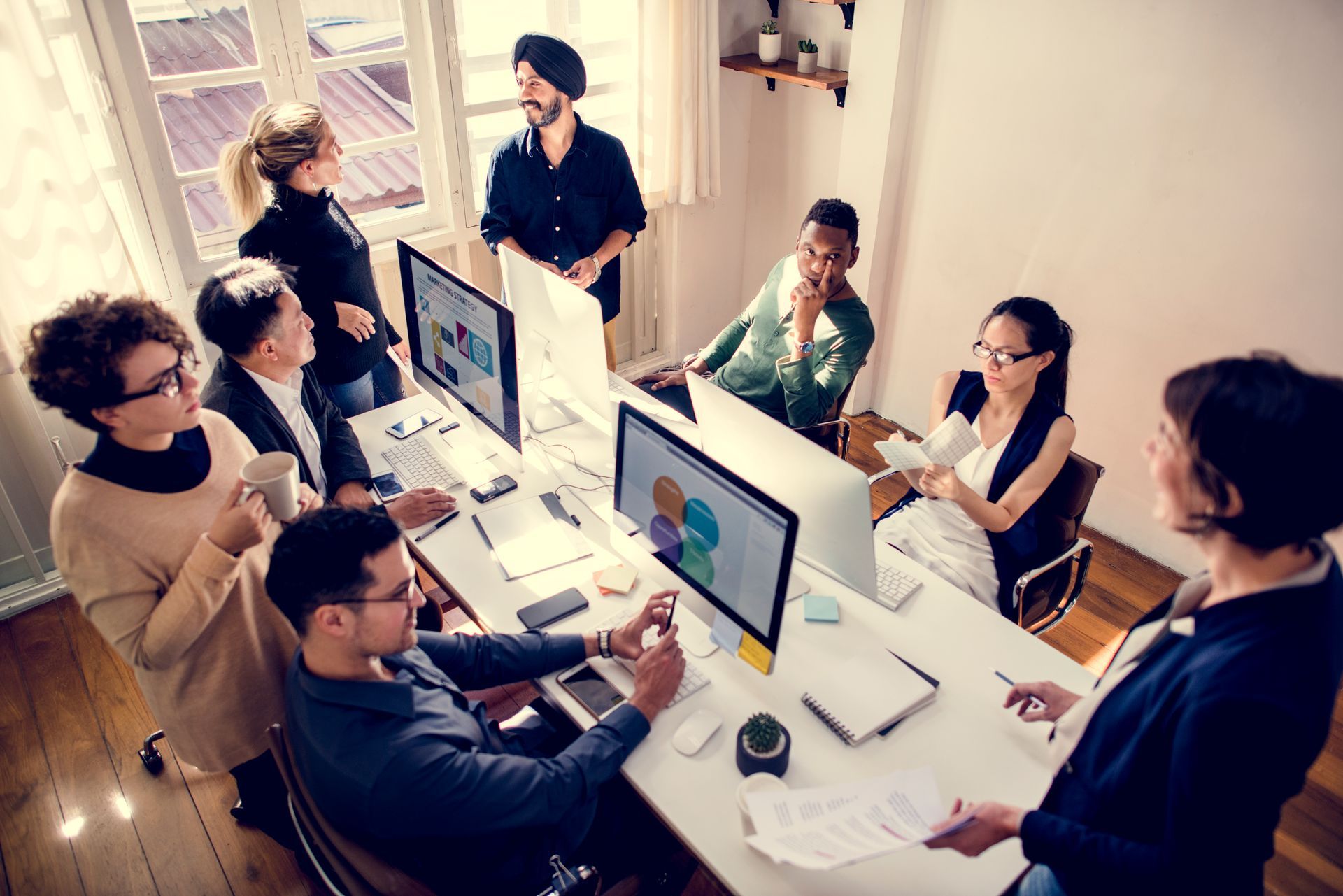 People in an office collaborating, viewing computer screens, discussing. Bright, natural lighting.