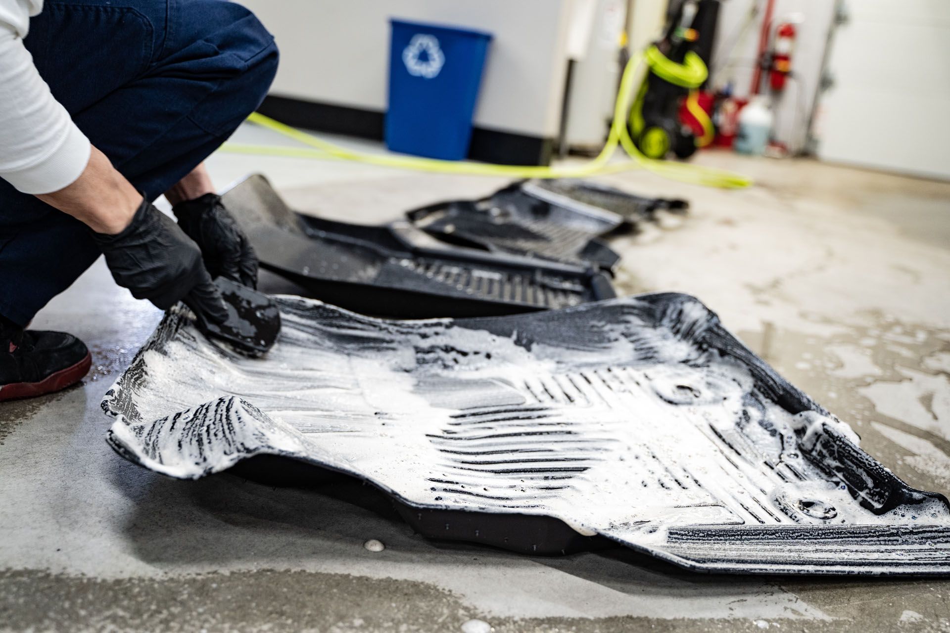 A person is kneeling down to clean a car mat in a garage.