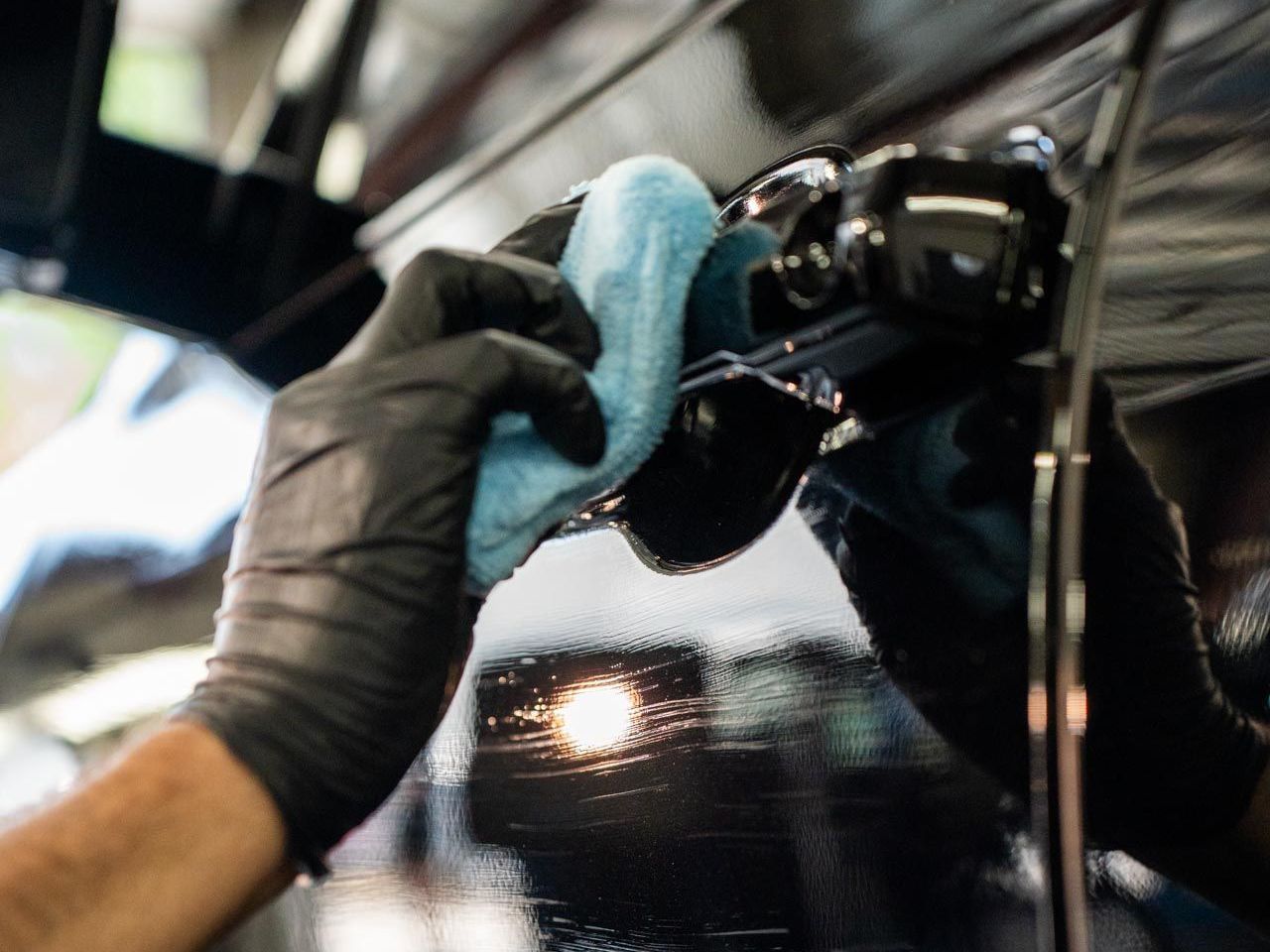 Gloved hand wiping a black car's side mirror with a blue cloth