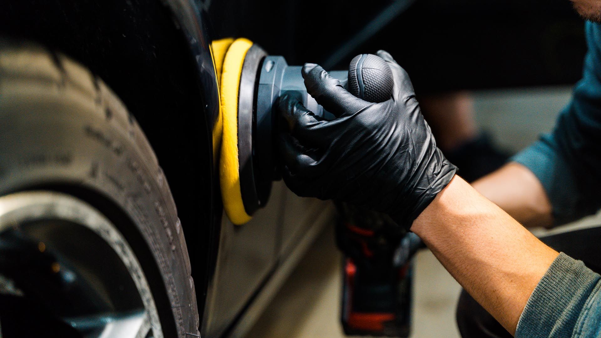 A man wearing black gloves is polishing a car with a machine.