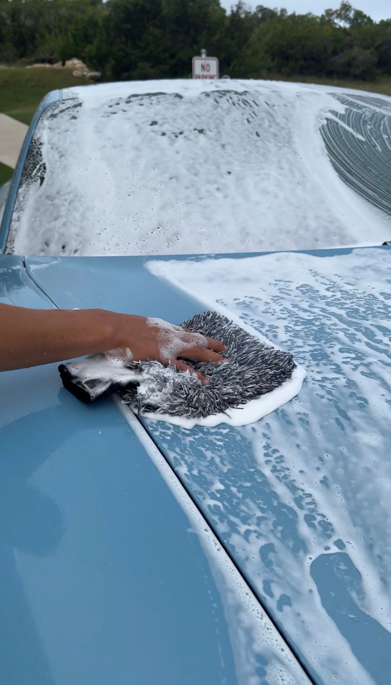 Person in blue gloves applying product to white car's headlight with a detailing applicator and spray bottle.
