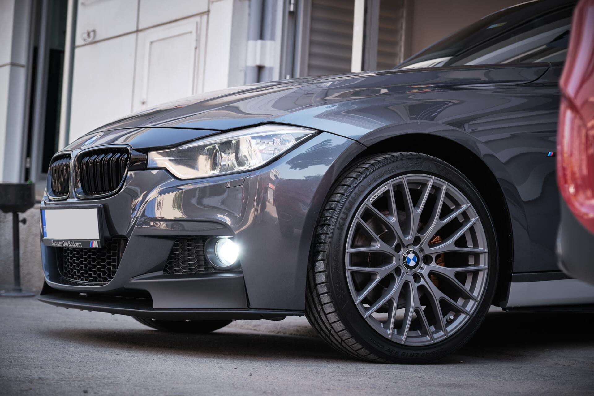 Gray BMW sedan parked in a garage, front view with headlights on