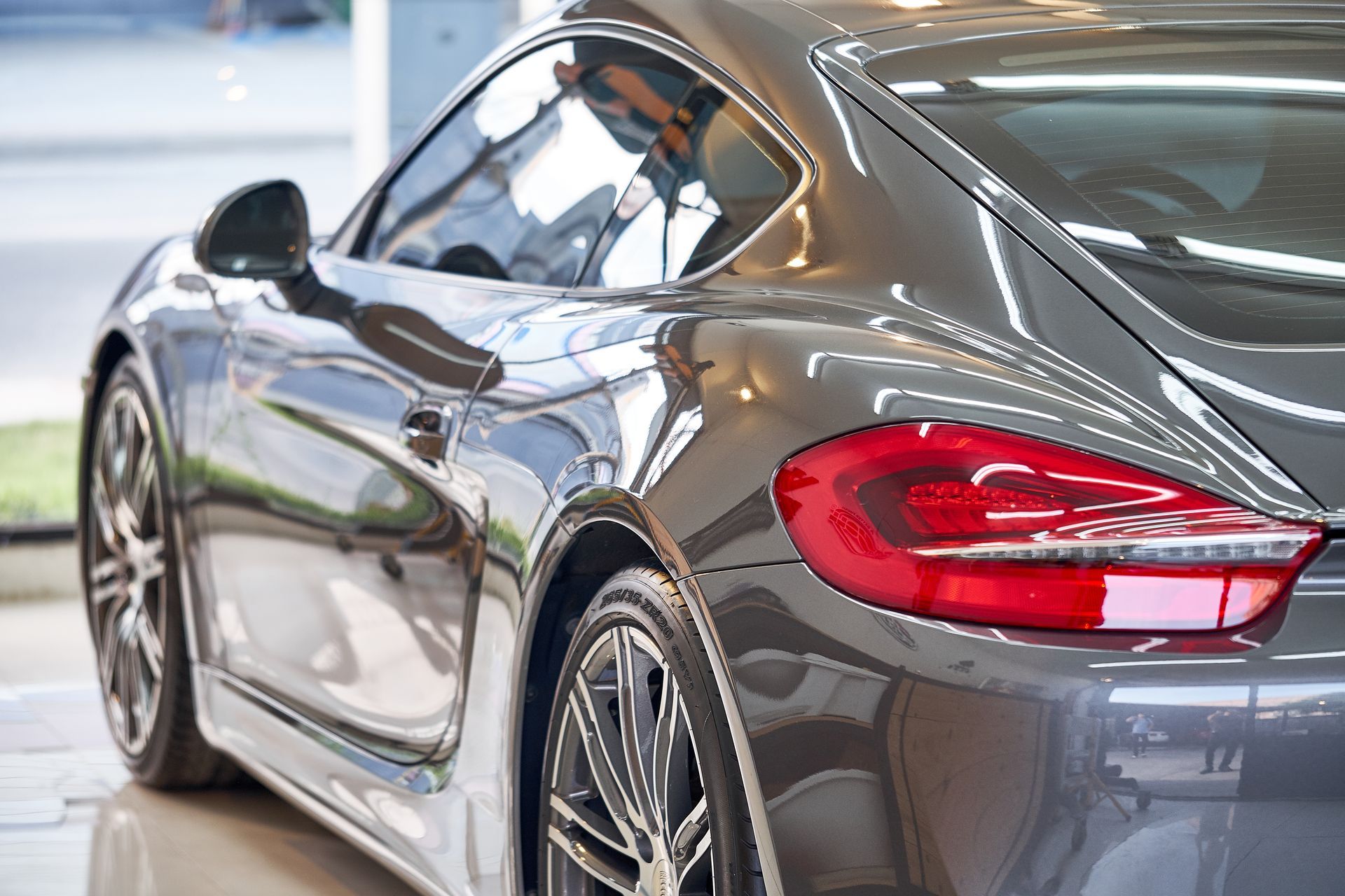 Rear three-quarter view of a metallic gray sports car in a showroom, highlighting the rear light and side profile