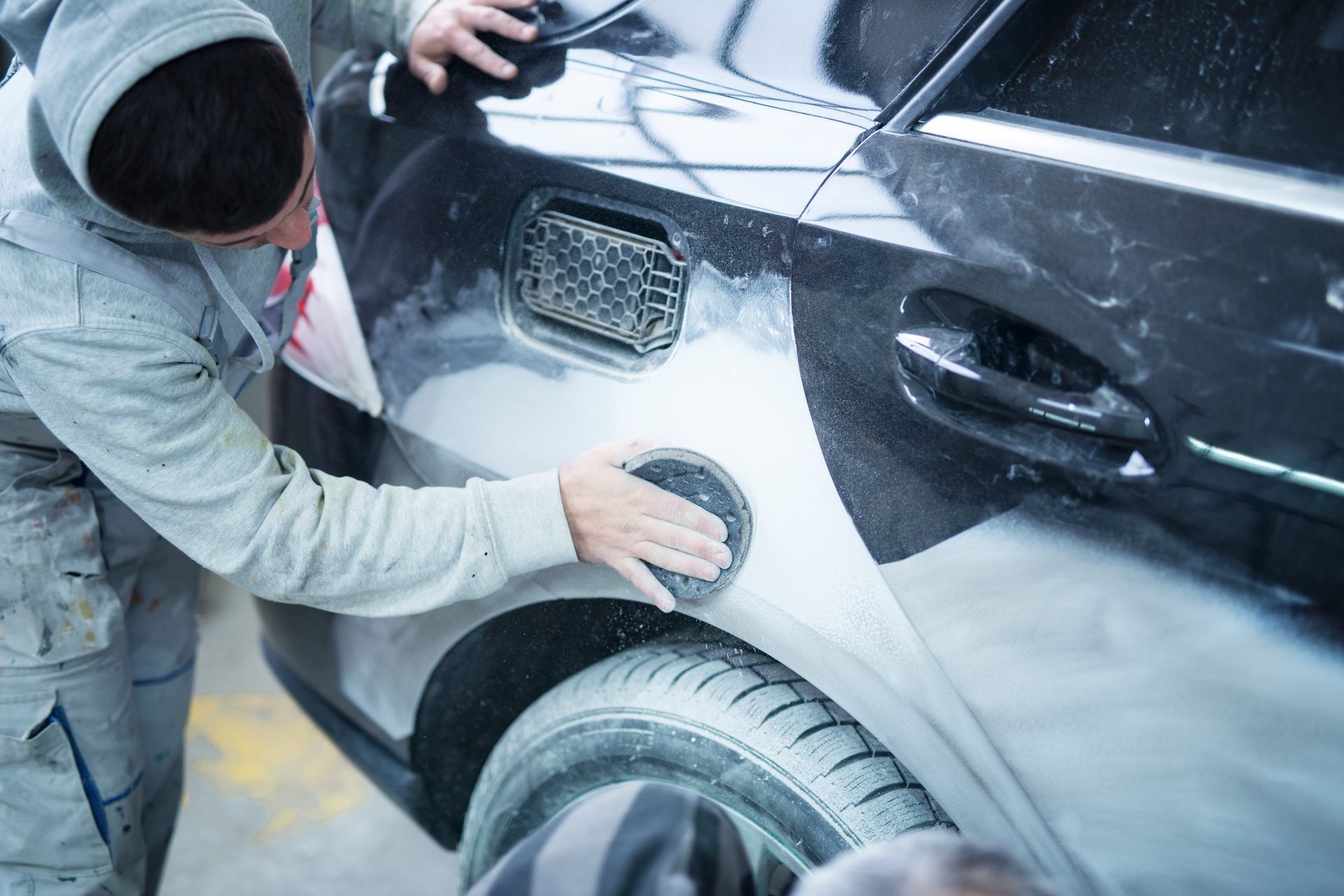 A man is polishing the side of a car with a sponge.