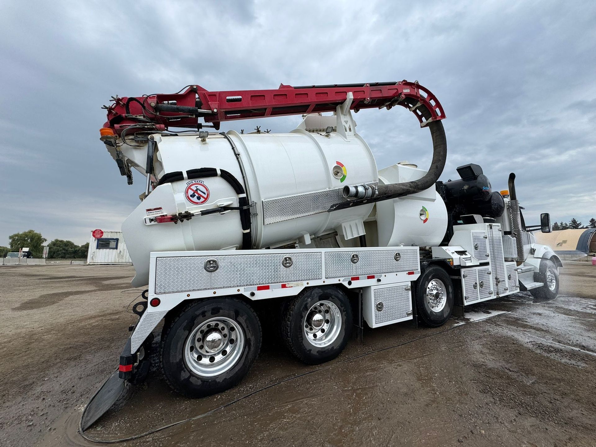 White vacuum truck on a cloudy day, with a red arm and large tank.