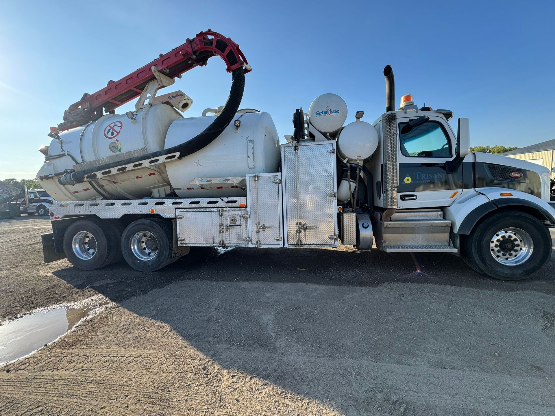 White vacuum truck parked on gravel, red hose extended upward.