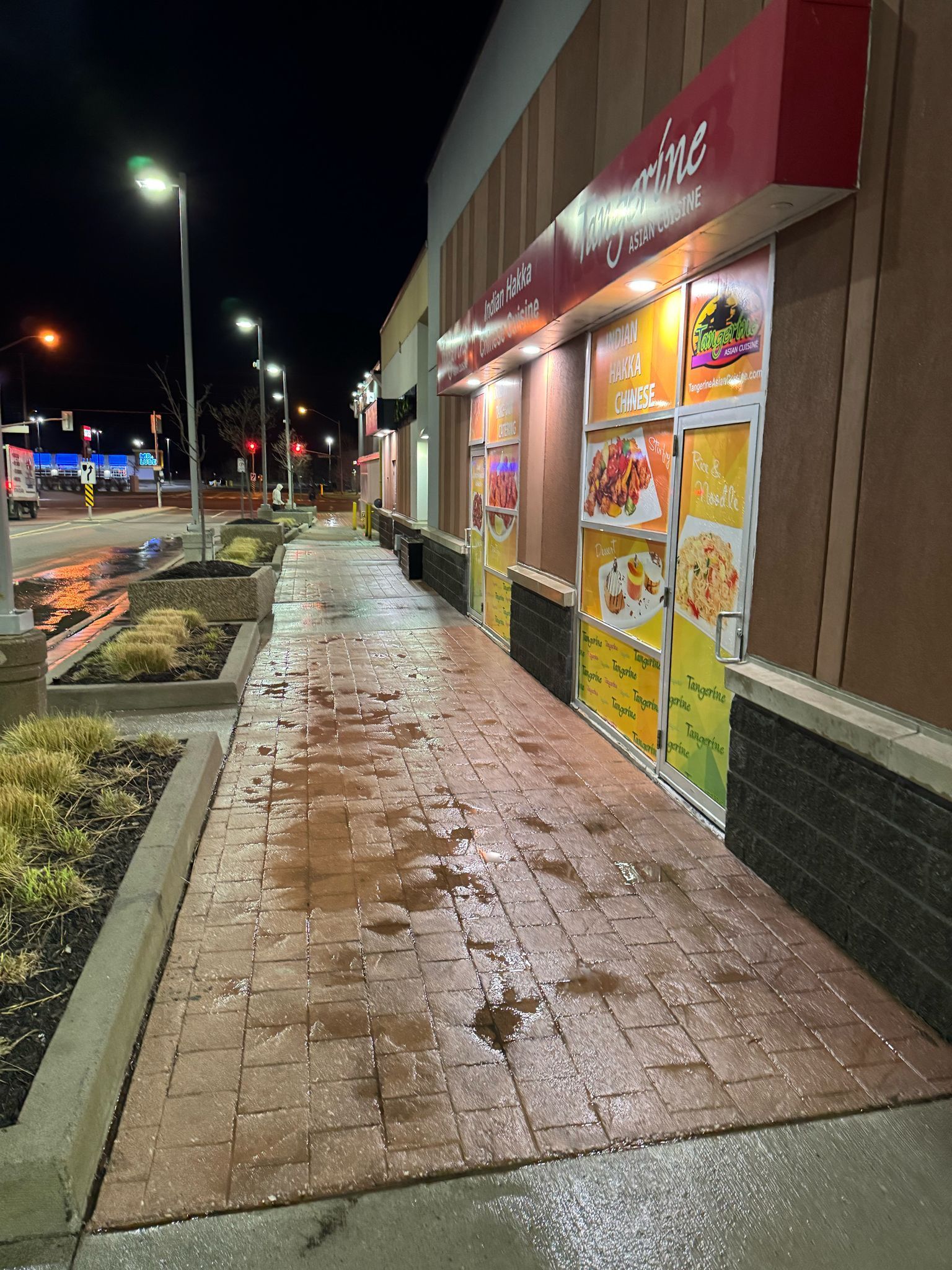 Exterior of a restaurant at night with a wet brick sidewalk.
