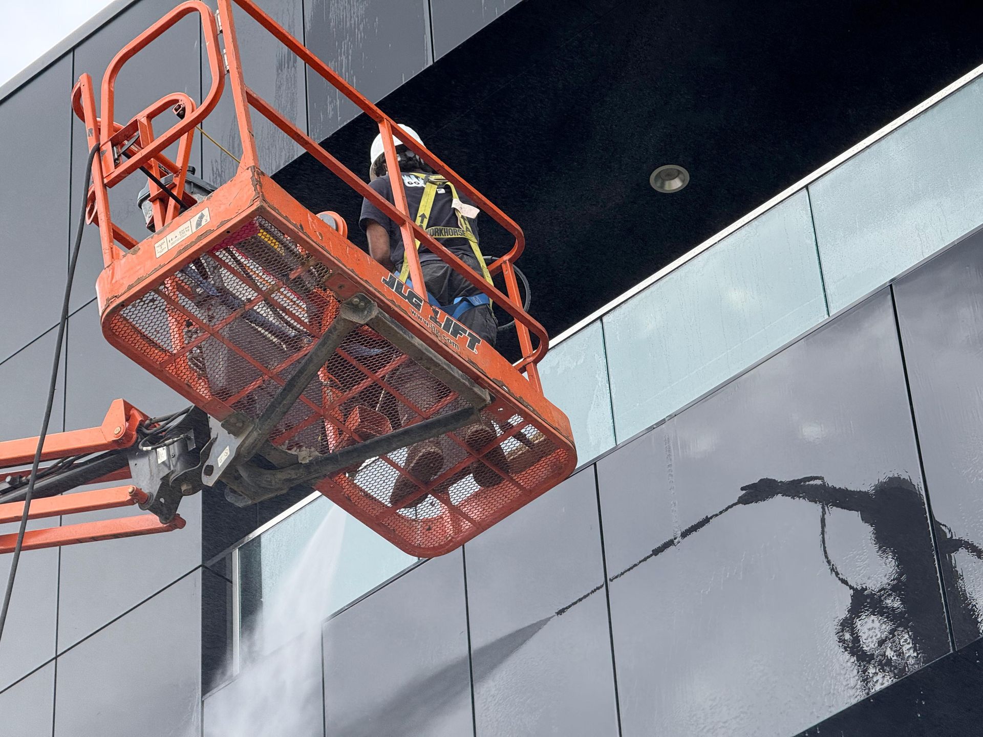Worker in orange lift washing the facade of a dark building. Water spraying downward.