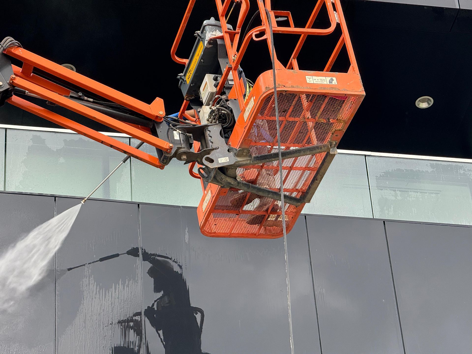 Orange lift platform spraying water on dark building facade.