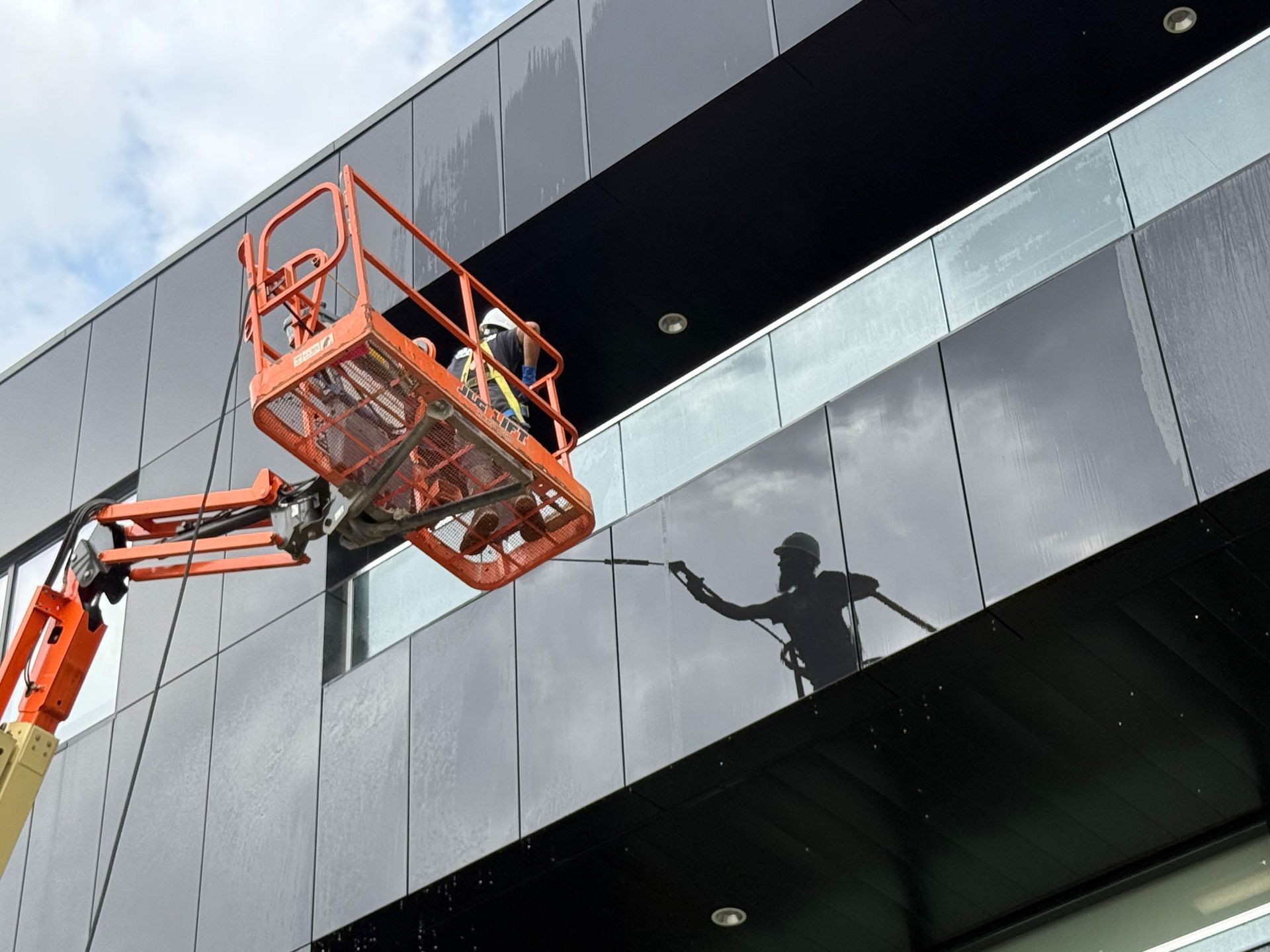 Worker in a lift washing black building facade with glass windows.