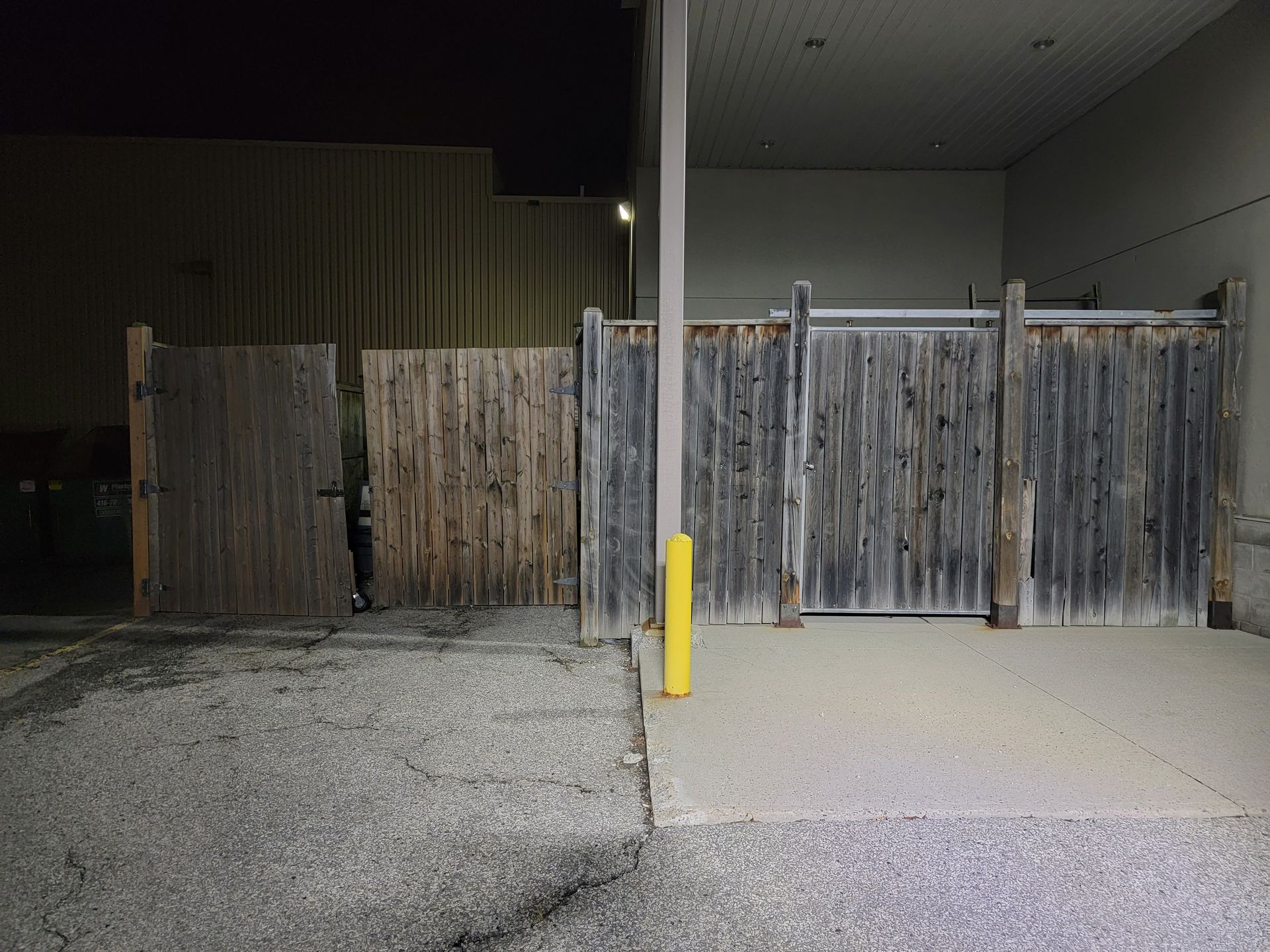 Wooden fence and gate near a building, on a paved area, at night.