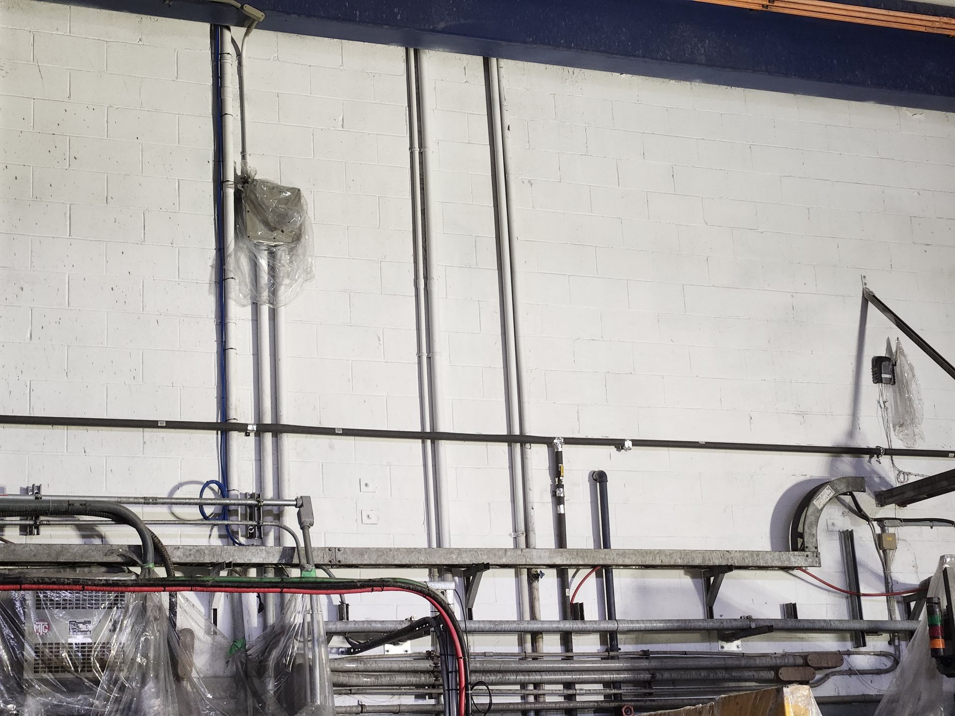 Industrial interior with pipes and cables against a white wall.