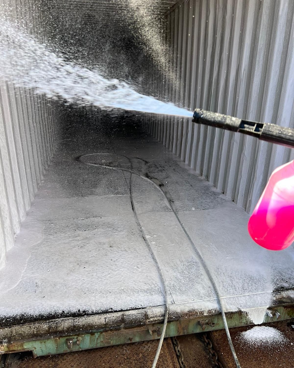 A person power washing the interior of a shipping container with soapy water.