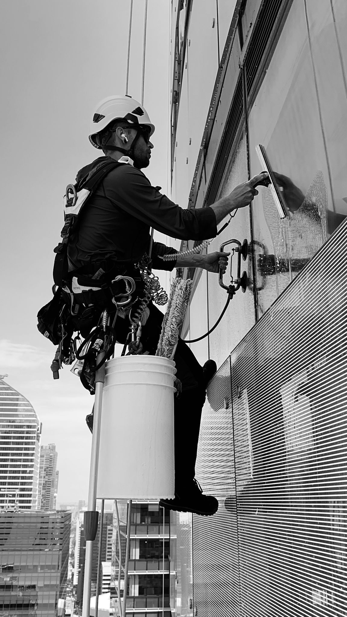 Window washer hanging on a tall building, cleaning a window with a squeegee.