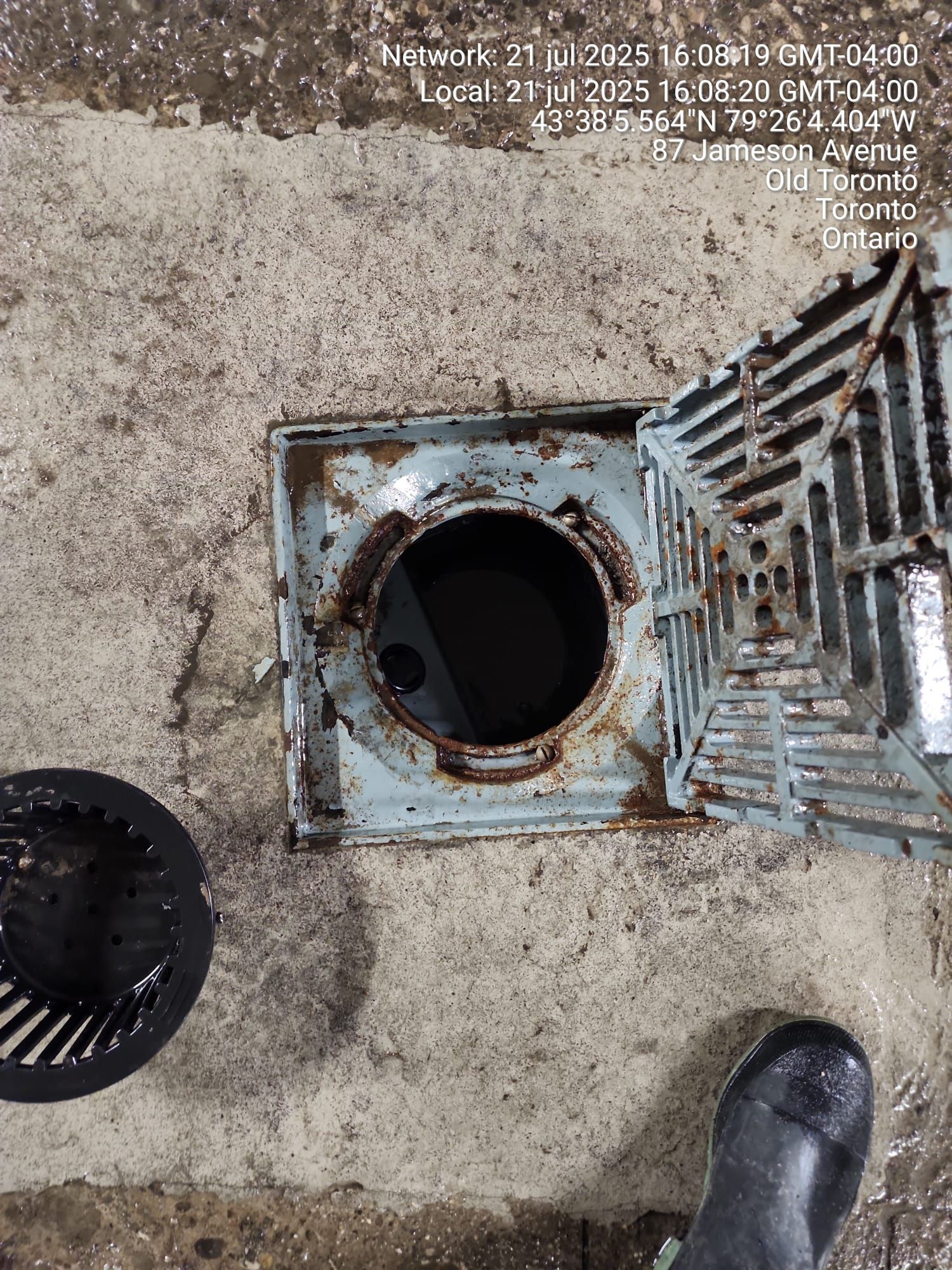 Open metal drain cover with dark hole in concrete ground.