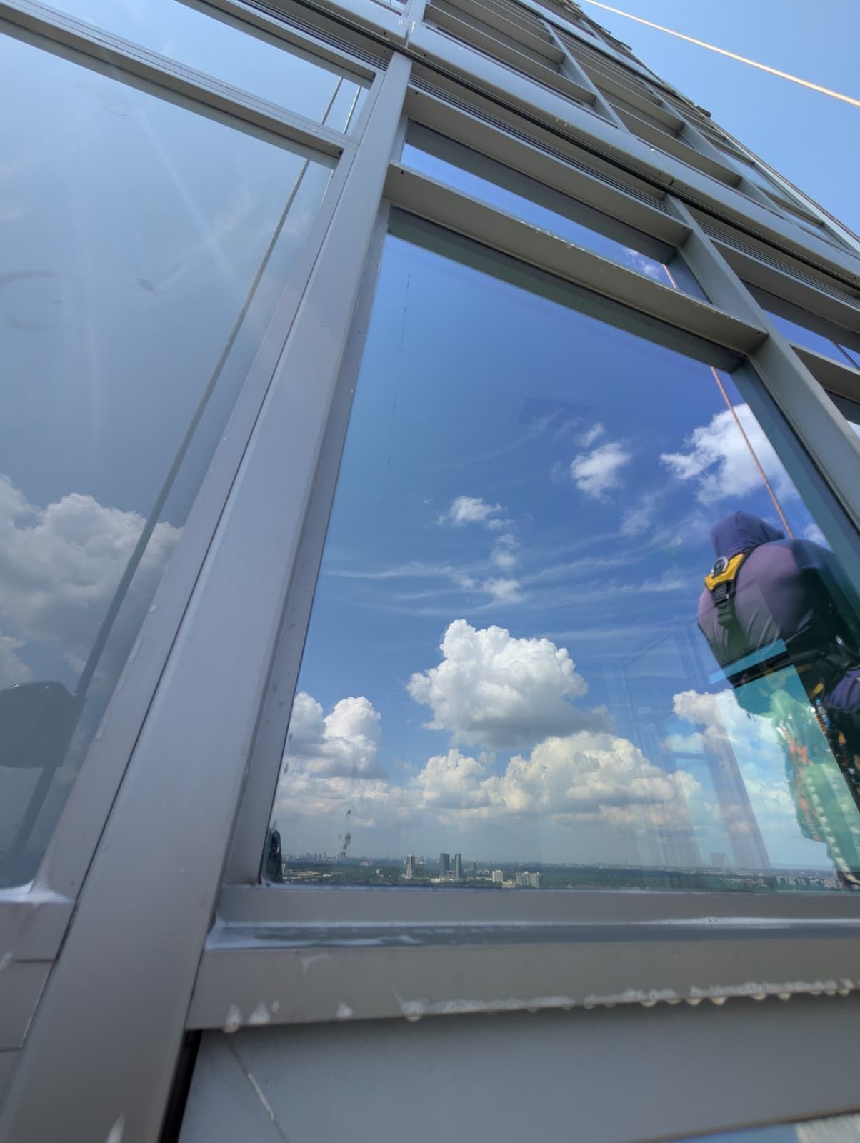 Tall building exterior. A window reflects the blue sky and clouds. A person in purple is also reflected.