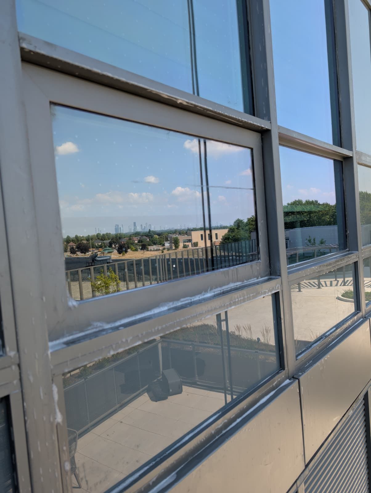 Exterior building windows reflecting a sunny sky and distant cityscape.