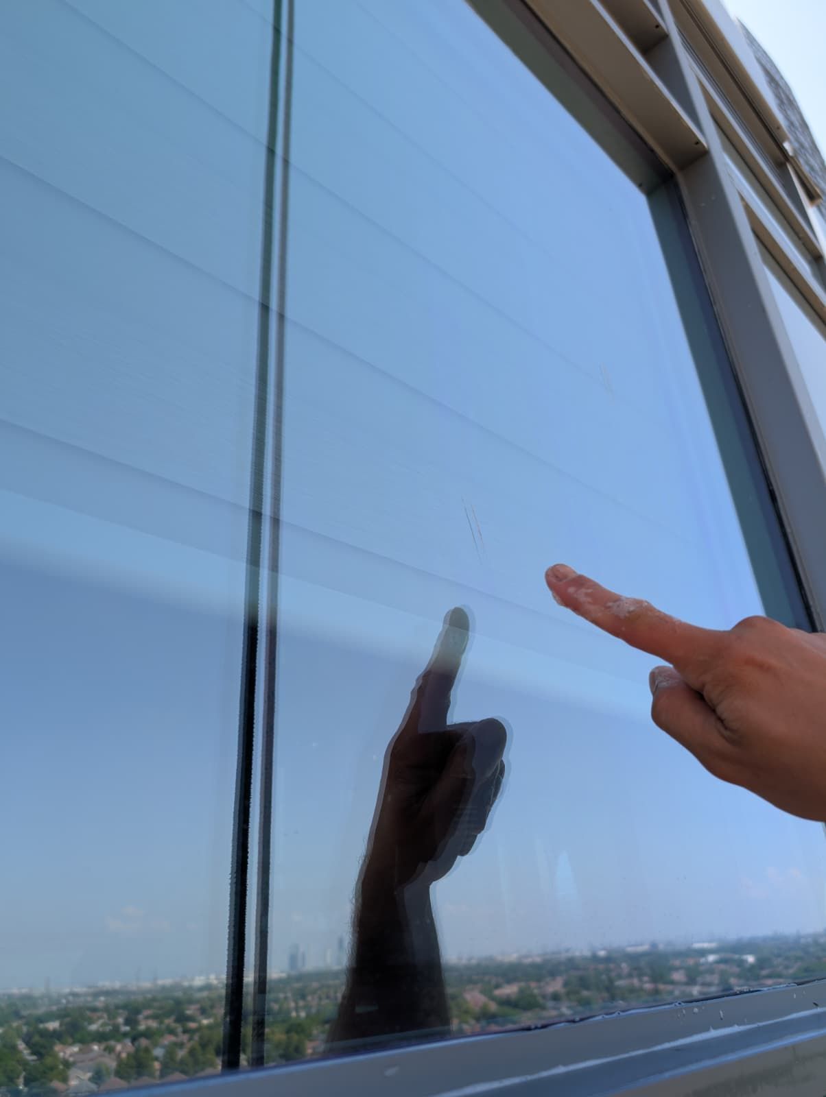Hand pointing at a window, with a reflection of the hand and a cityscape visible through the glass.