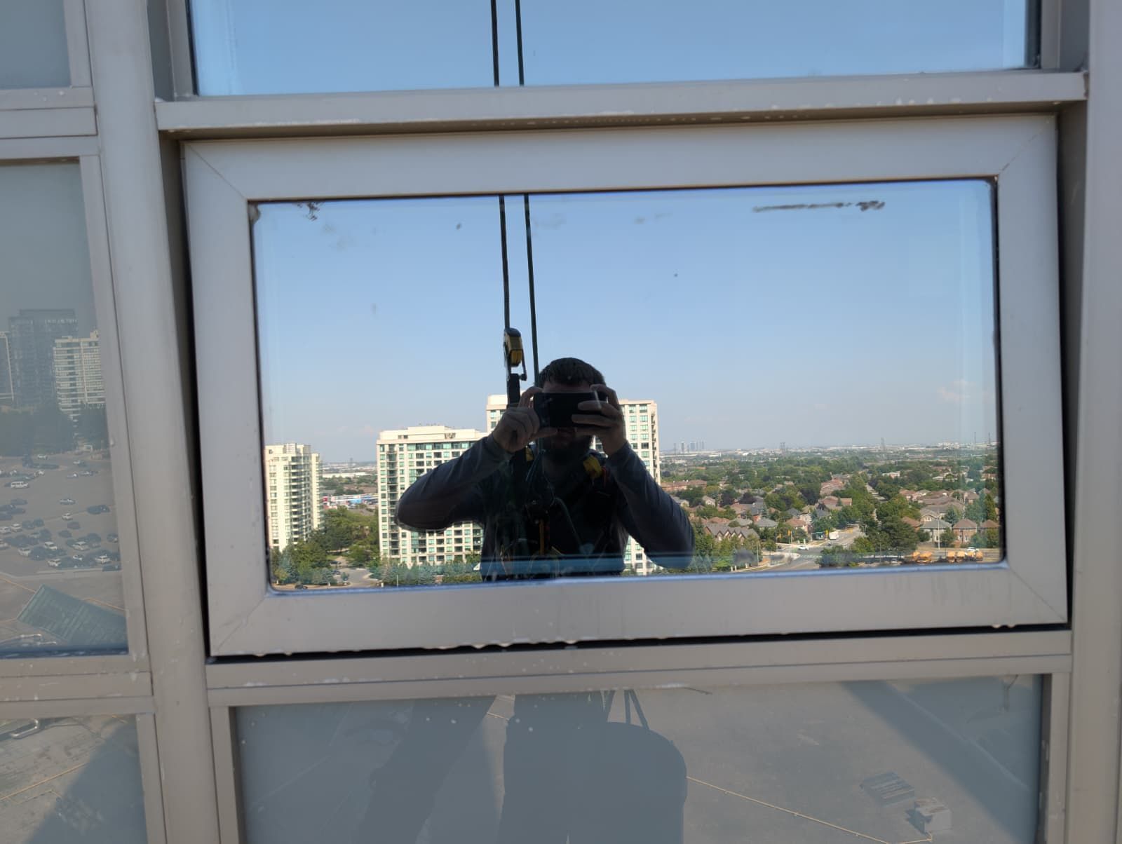 Reflection in window shows person taking photo of city skyline and buildings.