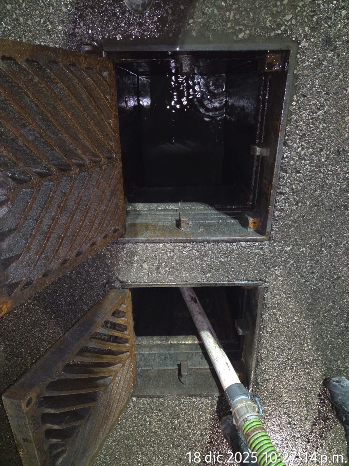 Open sewer access, rusty metal, dark interior, hose inserted, water droplets.