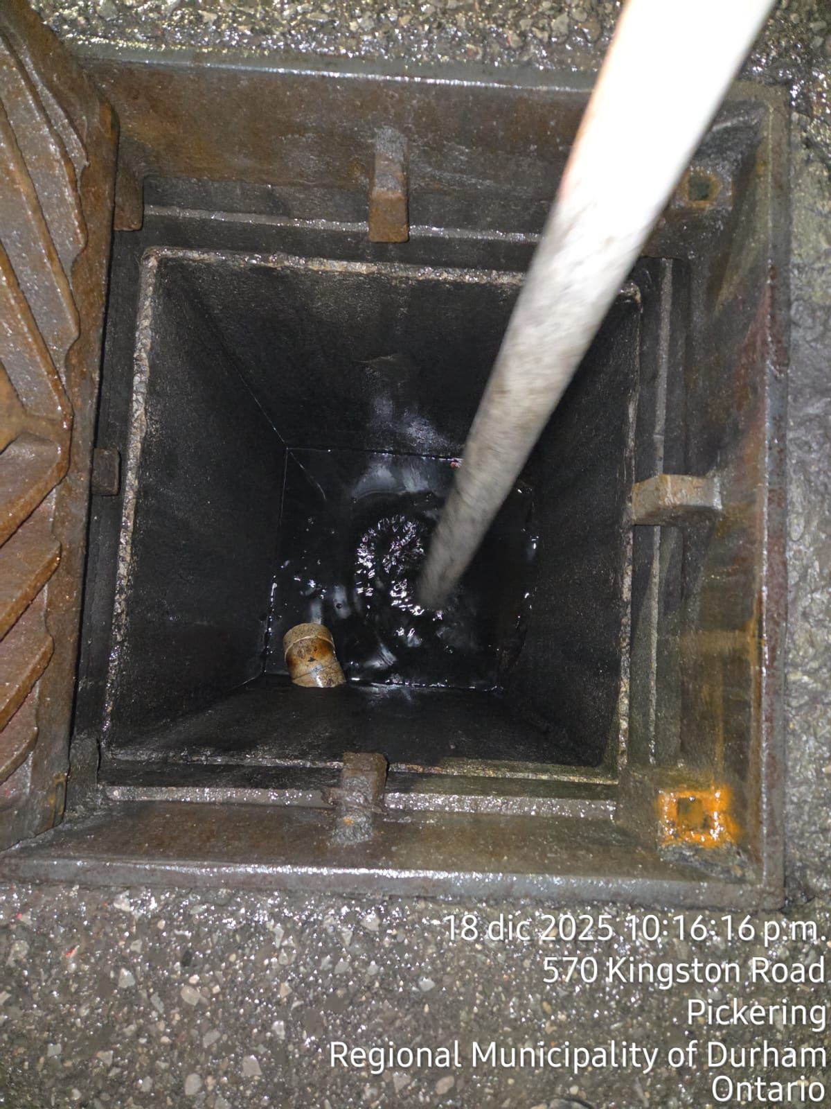 Looking down a dark sewer drain with a pole inside; location 570 Kingston Road, Pickering.