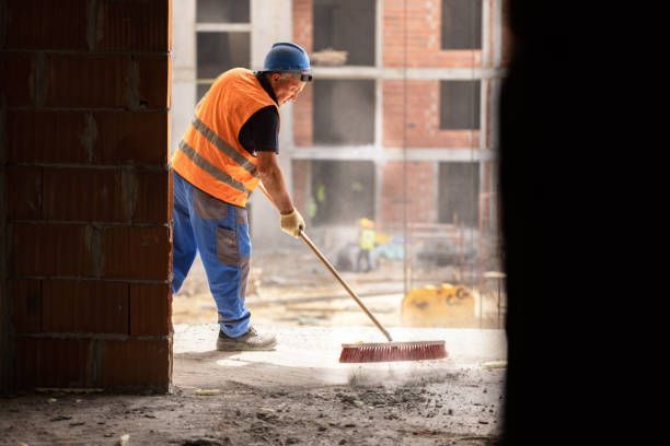 Construction worker sweeping inside a building, wearing safety vest and blue pants.