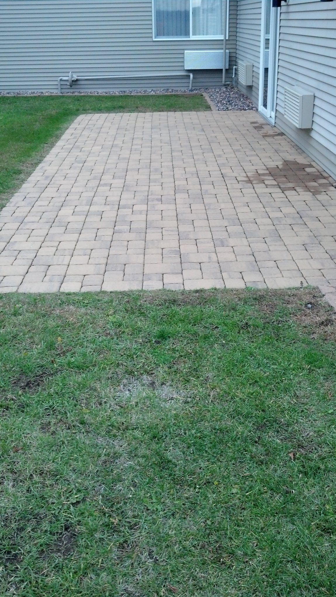 Brick patio next to a building with a window and a door, surrounded by green grass.