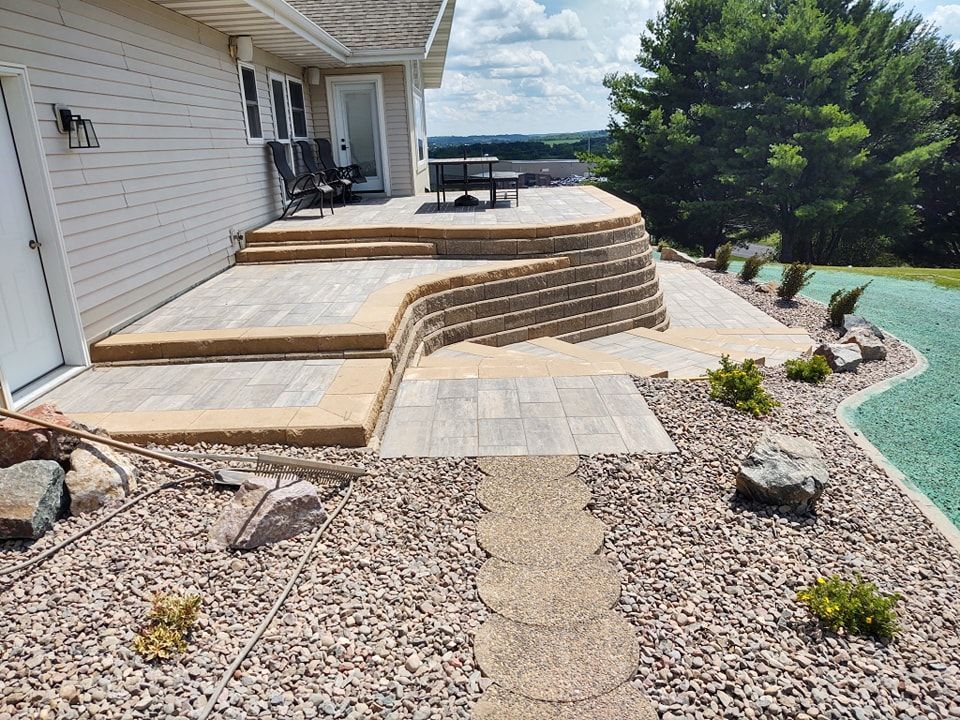 Stone patio with terraced levels and steps, surrounded by landscaping, overlooking a distant vista.
