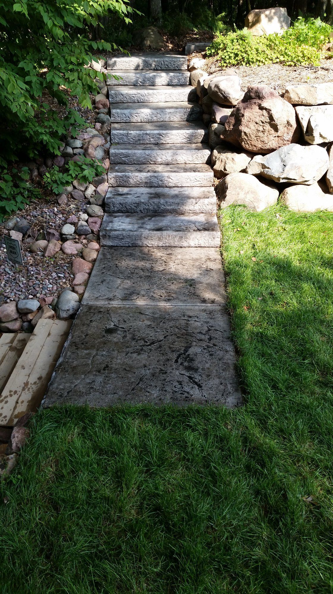 Stone steps and walkway leading up a hill through a yard with green grass and foliage.