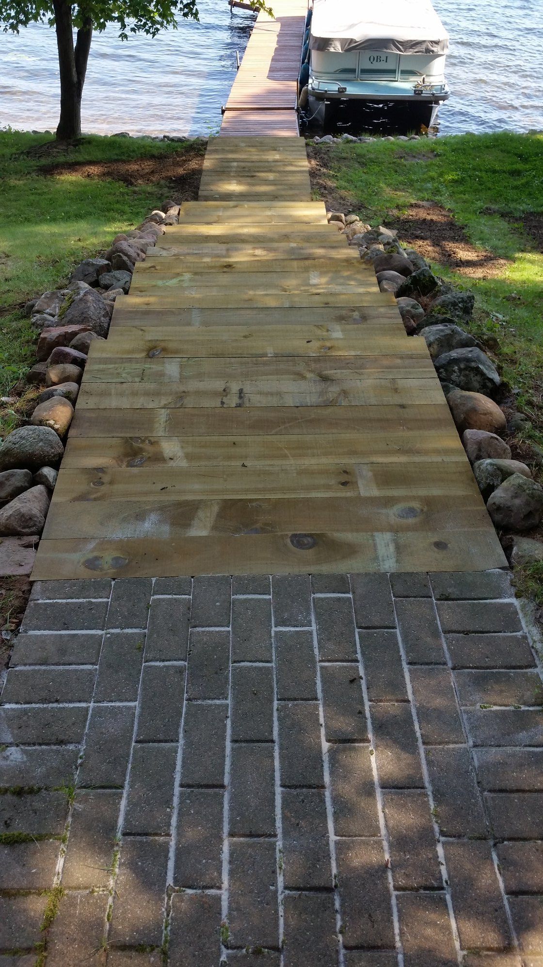 Brick path leads to wooden stairs down to a dock with a boat on a lake.