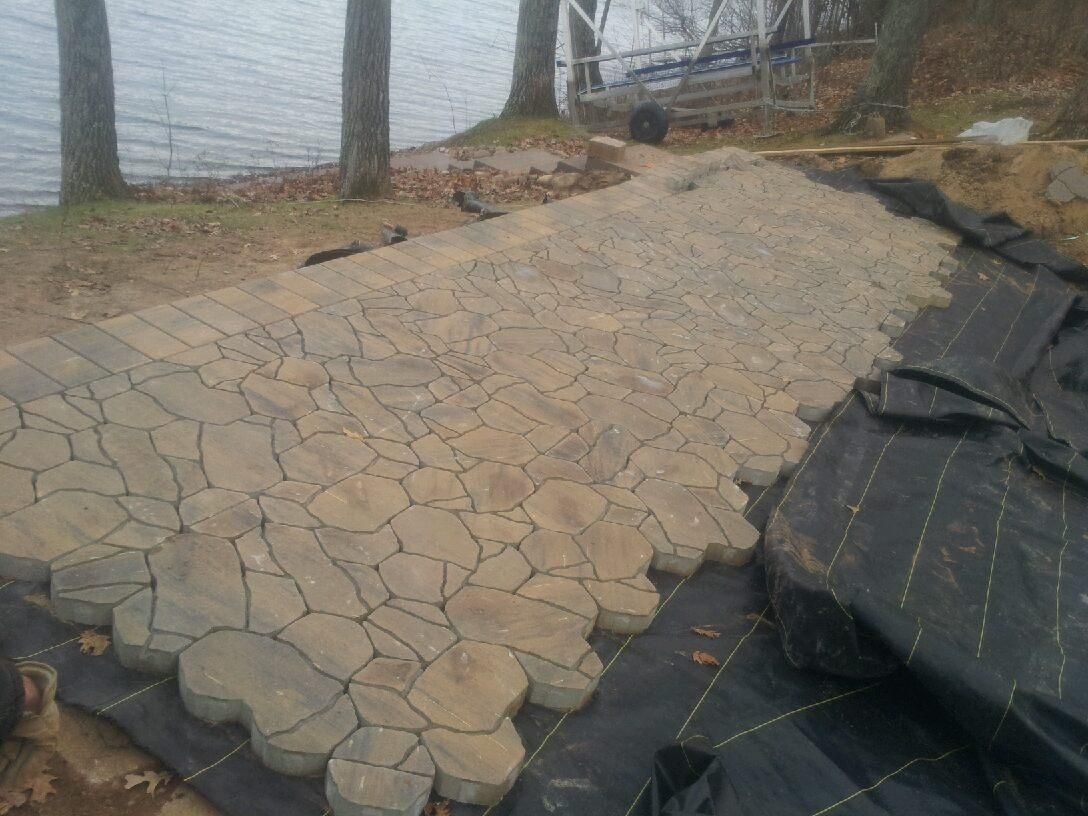 Pathway under construction, composed of irregular stone pavers, leading to a body of water.