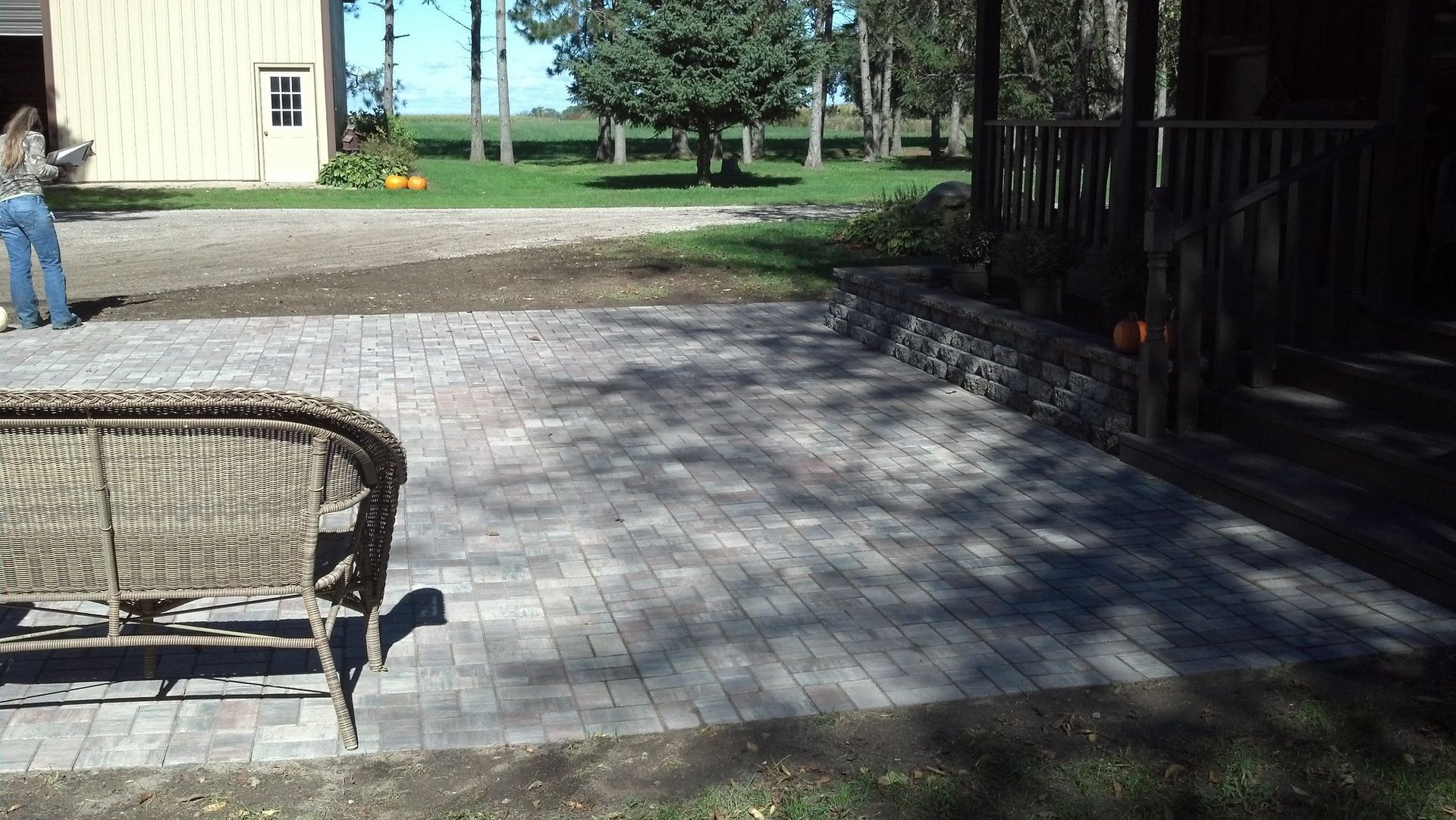 Brick patio beside a house with a person standing nearby. Sunny day.