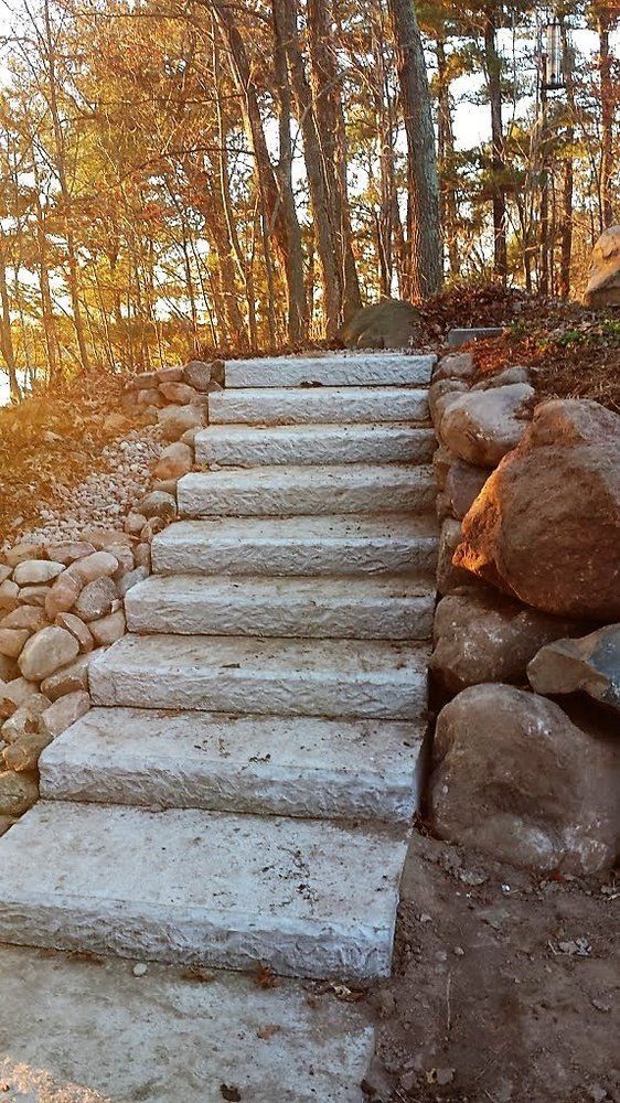 Stone steps ascend a hillside, flanked by rocks and leading into a wooded area.