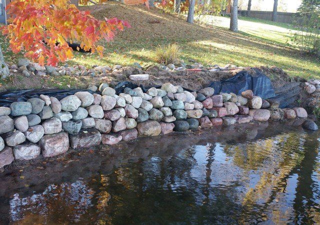 Stone retaining wall along a pond, autumn leaves in background.