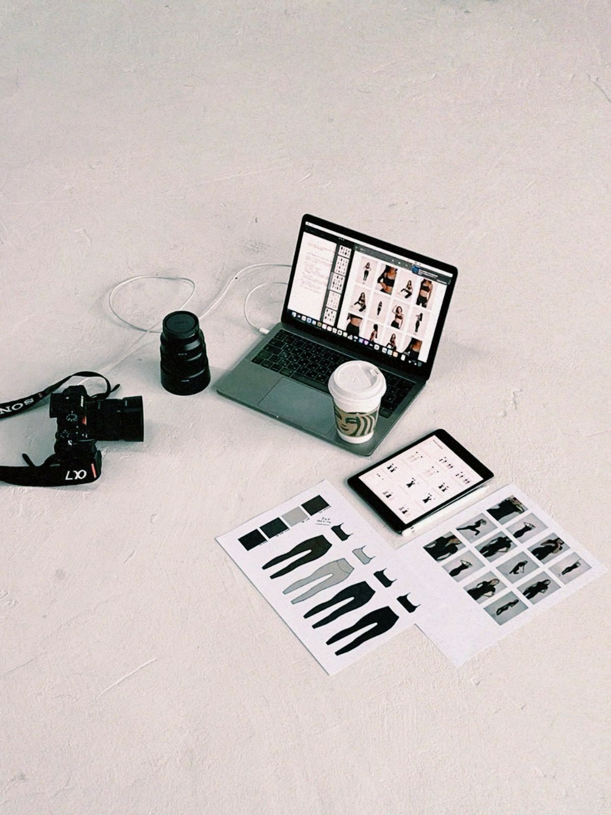 Laptop, tablet, camera, and printouts on a white surface.
