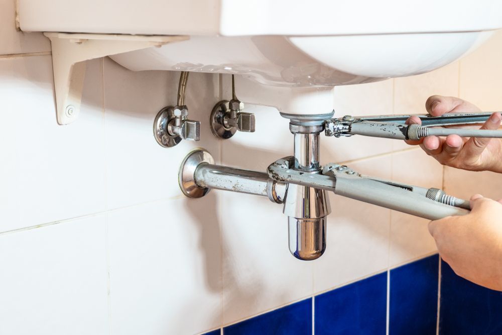 Hands Using a Wrench to Tighten or Repair a Metal Sink Drain Pipe — PlumbPlus in Kawana, QLD