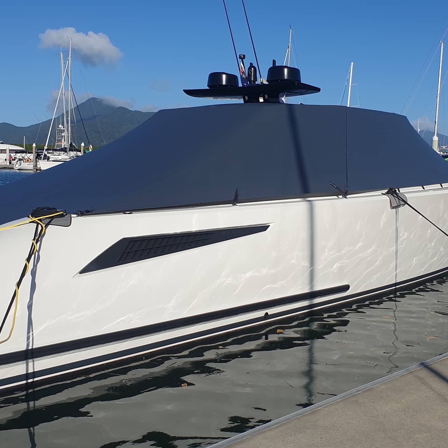 A White Boat With a Black Cover is Docked in the Water — Coastal Coverings In Redlynch, QLD