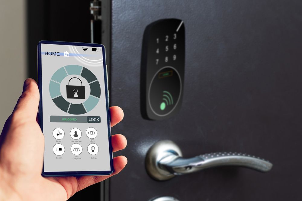 A person is holding a smart phone in front of a smart door lock.