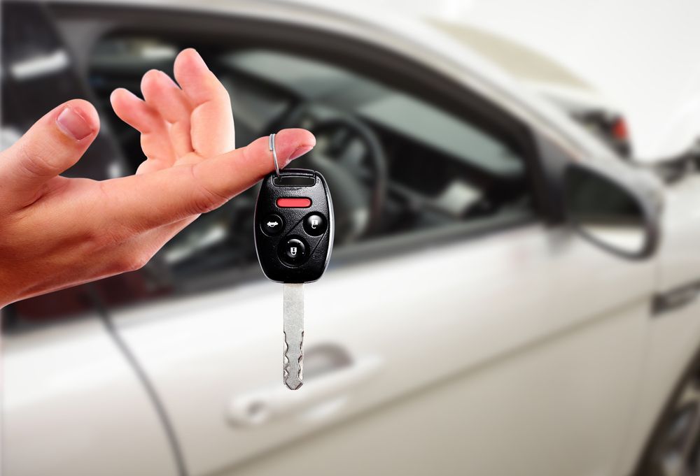 A person is holding a car key in front of a car