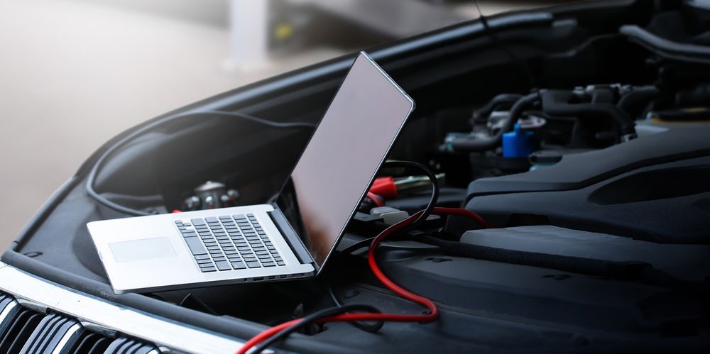 A laptop is sitting under the hood of a car.