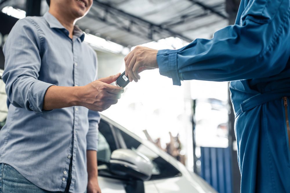 A man is handing a car key to a mechanic in a garage.