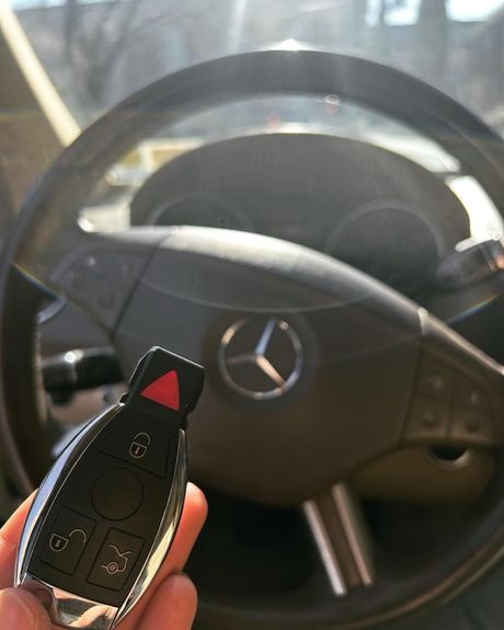 A person is holding a mercedes key in front of a steering wheel